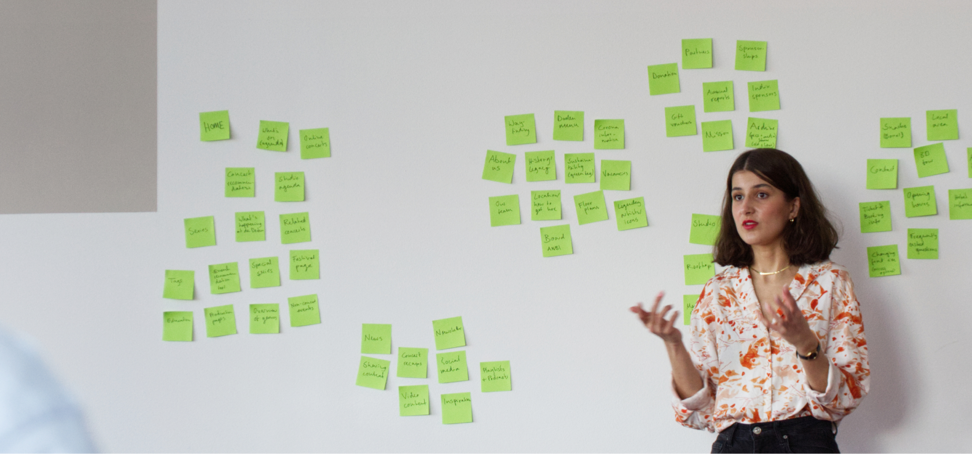 Julia is standing in front of a wall of green post it notes, presenting a Discovery workshop.